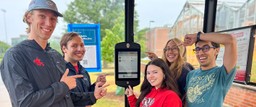 Students pose in front of a solar-powered bus schedule panel.