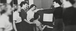 Members of Groves gathered around a piano.
