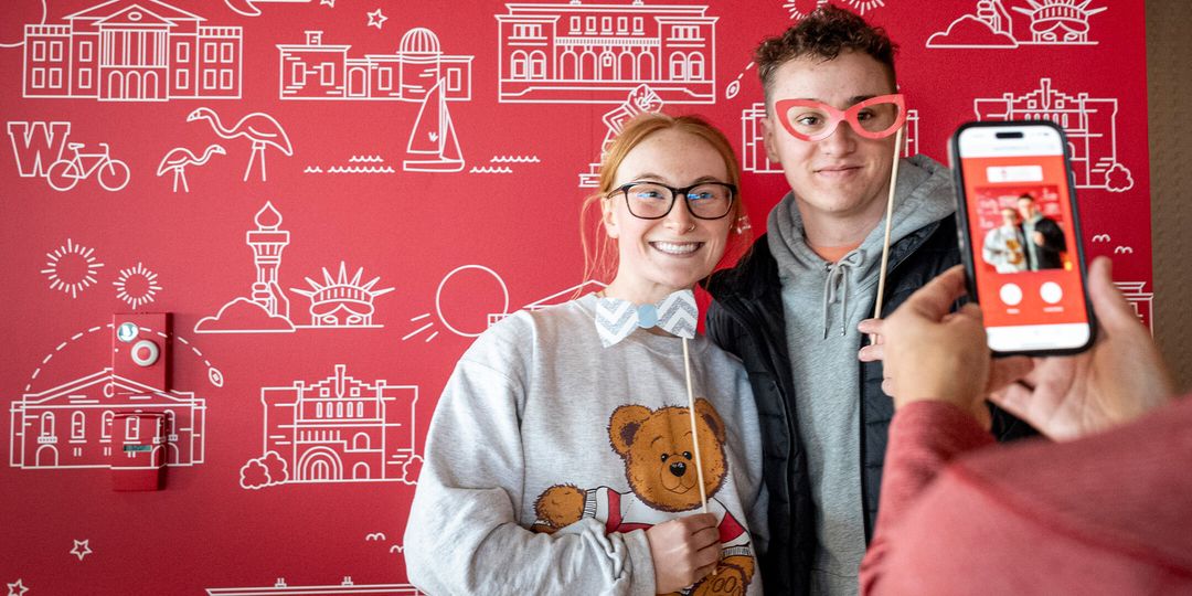 Two people pose for a picture; background consists of UW icons