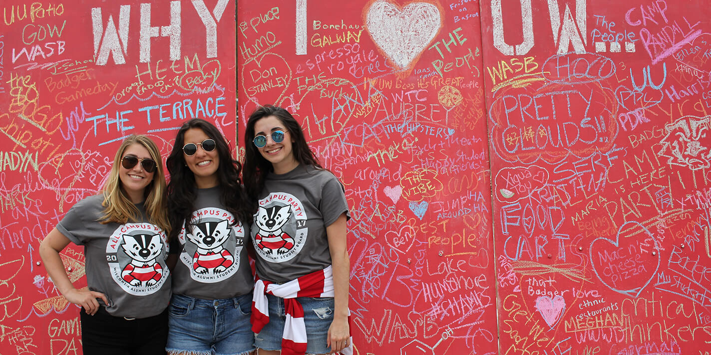 Three WASB students in front of "Why I heart UW" graffiti board