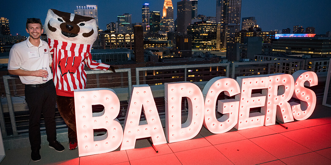 Bucky and an alumnus pose beside the word "BADGERS" lit up with light bulbs.