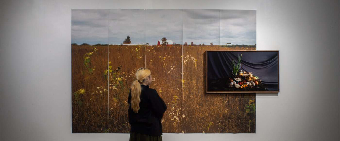 A woman with a blonde ponytail dressed in black looks at art on the wall of an art gallery.