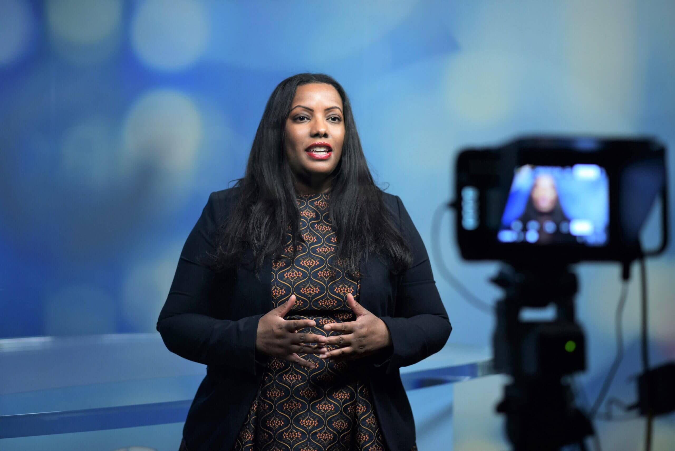 Dana Peterson stands in front of a camera in a studio while presenting.